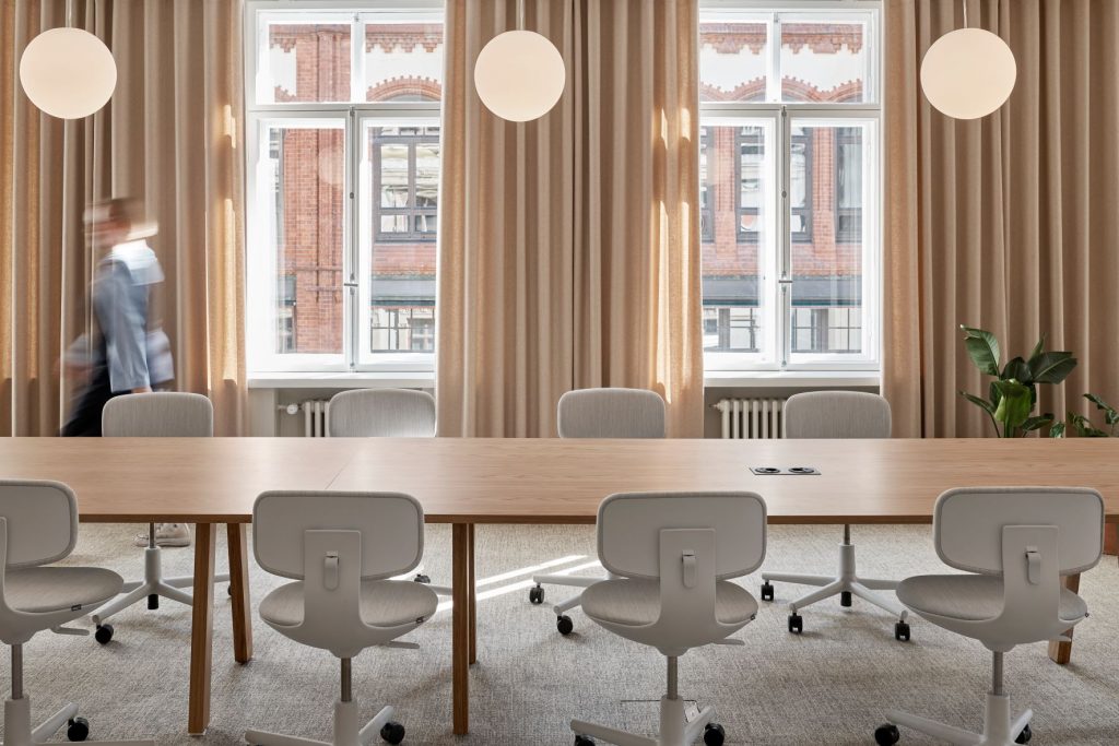 Toimiston neuvotteluhuone, jossa on pitkä pöytä ja Fabrican palotruvalliset, beiget, vaaleat verhot